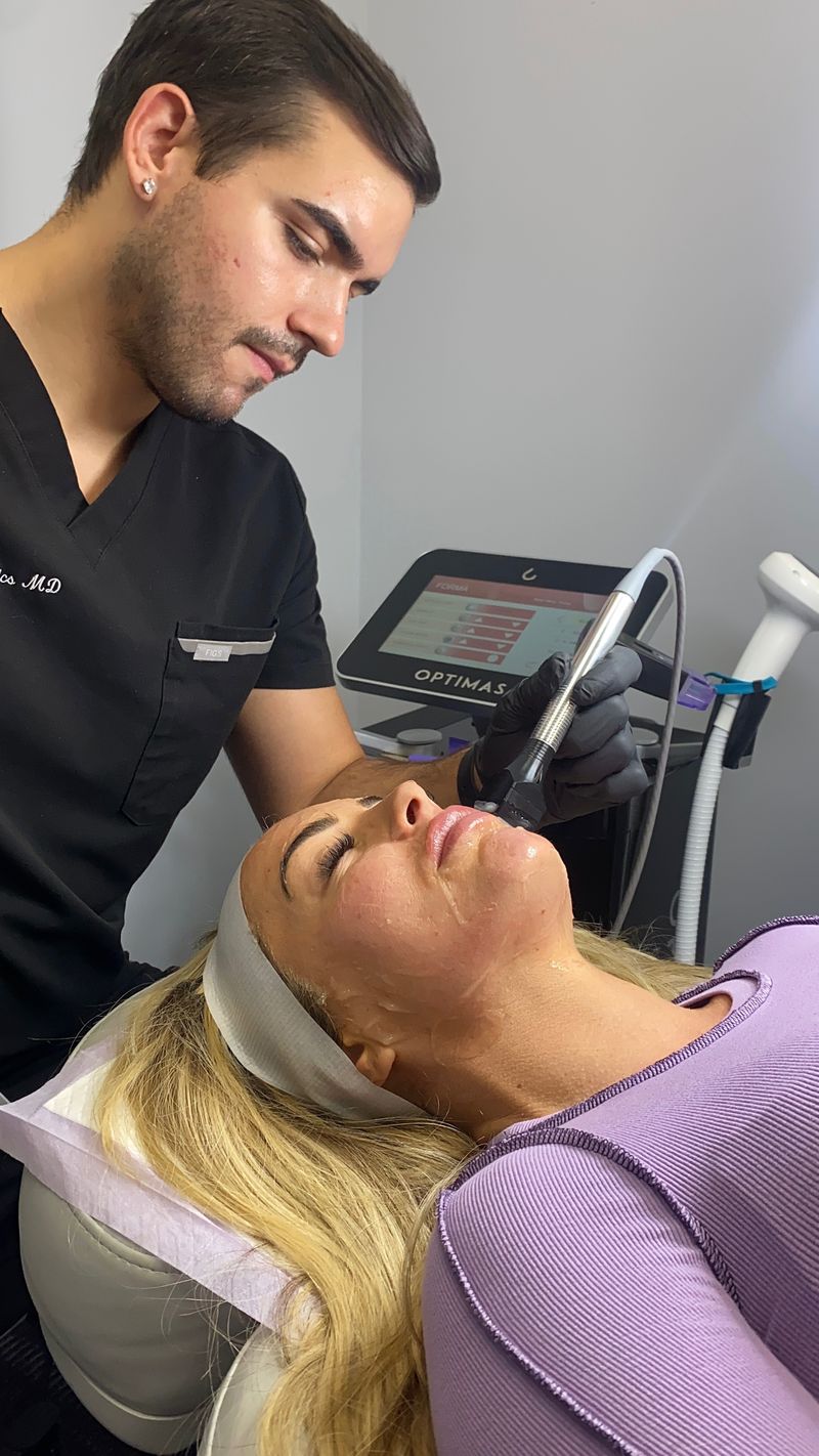 A Forma radiofrequency handpiece gliding along a patient’s cheek beside the InMode console at Hudson Aesthetics MD