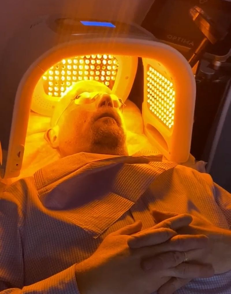 A patient resting beneath the amber glow of an LED light therapy panel at Hudson Aesthetics MD
