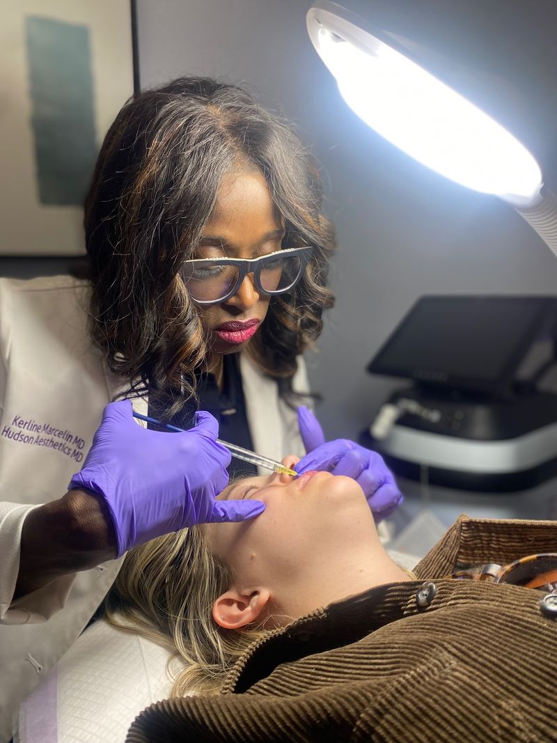 Dr. Kerline Marcelin injecting dermal filler into a patient’s lip under a ring light at Hudson Aesthetics MD